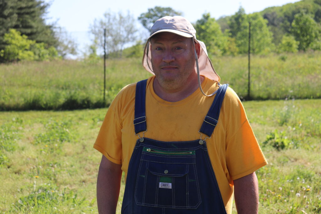 2022 Apprentice Charles wears a yellow shirt, blue overalls, and sun cap.