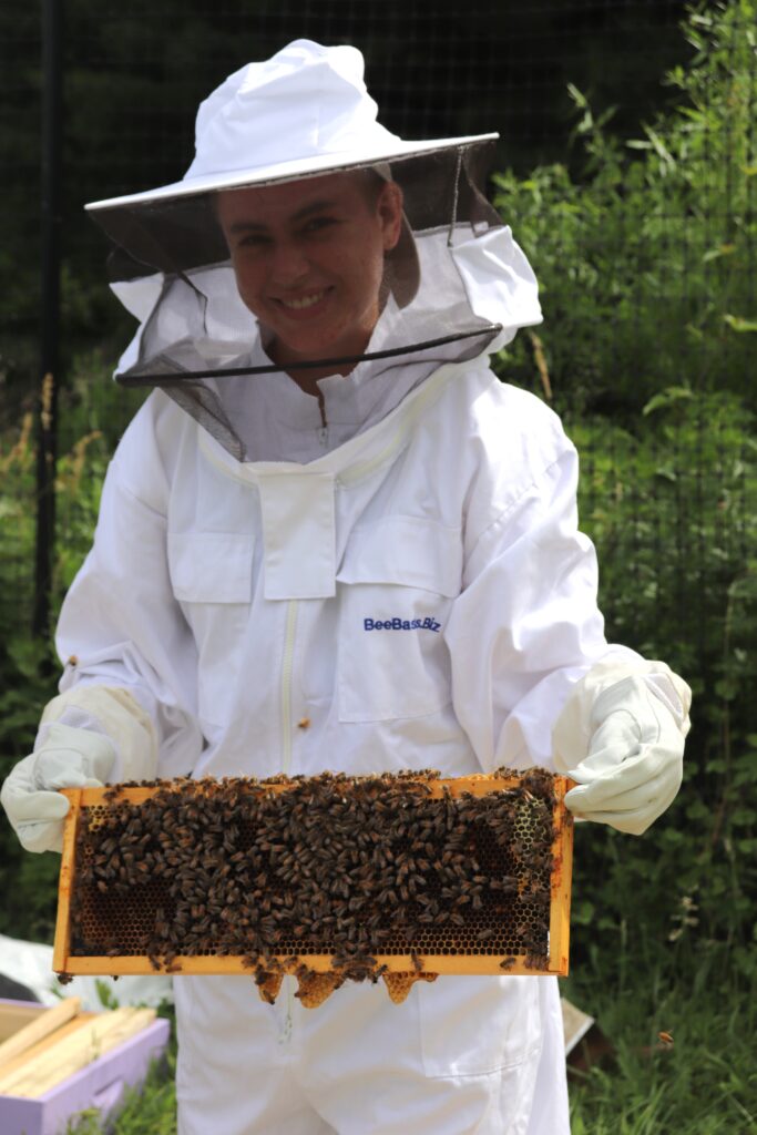 2022 Apprentice Laith in beekeeping suit holding a frame full of bees.